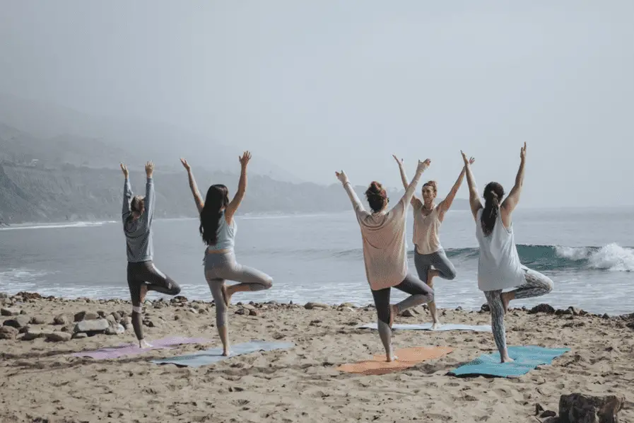 women are playing yoga on seaside